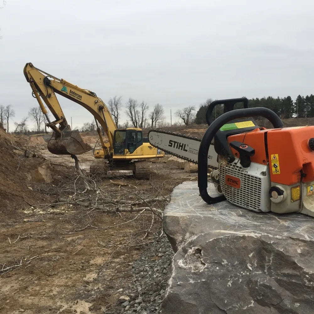 Professional chainsaw and heavy equipment on a tree clearing job site